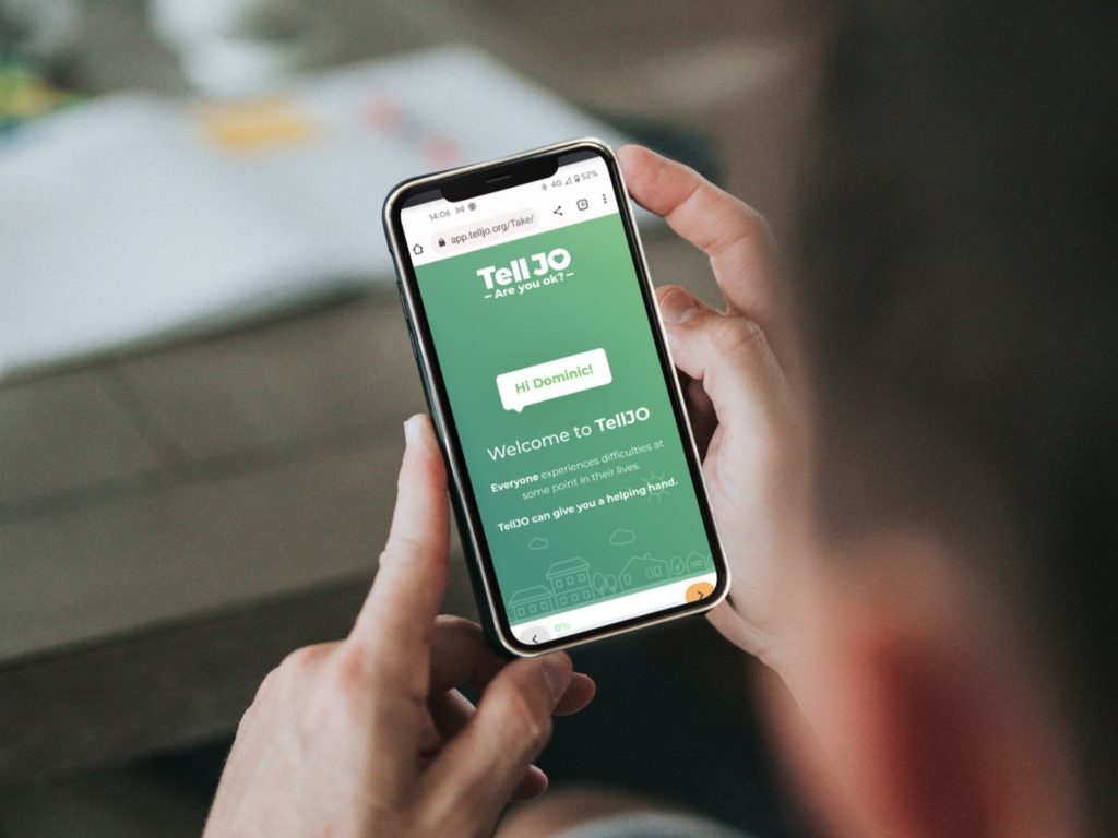 TellJO can help with the cost-of-living crisis and mental health issues. In the image a person is looking at a mobile phone showing a TellJO wellbeing check